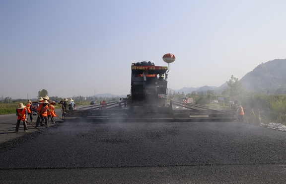 2019年8月，宜春經(jīng)開區(qū)S311路面攤鋪現(xiàn)場(chǎng)，工友們輔助路面兩側(cè)的分料、補(bǔ)窩等作業(yè)